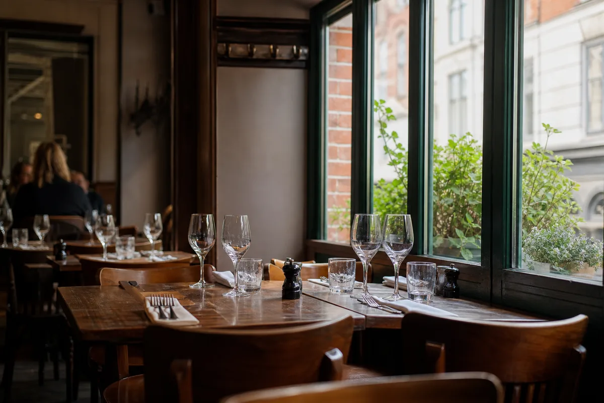 Salle de bistrot lilloise en service du midi, tables dressées près d&rsquo;une baie vitrée